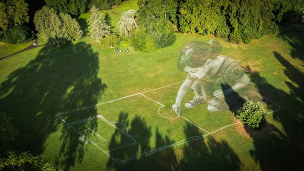 Aerial view of a giant girl drawing on the green field bathed in soft sunlight creating a whimsical scene against the backdrop of lush trees Gen&egrave;ve Gen&egrave;ve Switzerland.