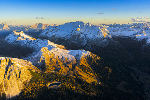 Aerial view of jagged snow dusted peaks kissed by golden sunlight contrasting with the deep shadows in the valleys below Marmolada Trentino South Tyrol and Veneto Italy.