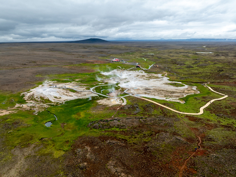 Aerial view of Hveravellir geothermal area with steaming vents wooden walkways and vibrant green moss set against a vast volcanic landscape in Hunabyggd Iceland.
