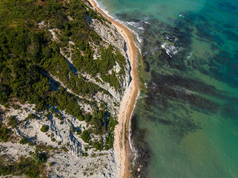 Aerial view of the Byala Cliffs featuring steep white rock formations lush green vegetation a narrow sandy beach and clear turquoise sea water in Byala Varna Bulgaria. Aerial view of the Byala Cliffs featuring steep white rock formations lush green vegetation a narrow sandy beach and clear turquoise sea water in Byala Varna Bulgaria.