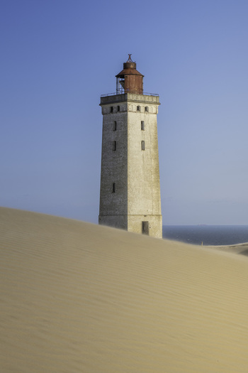 View of the historic Rubjerg Knude lighthouse rising above the vast sand dunes with the sea in the background in Lokken Denmark. View of the historic Rubjerg Knude lighthouse rising above the vast sand dunes with the sea in the background in Lokken Denmark.