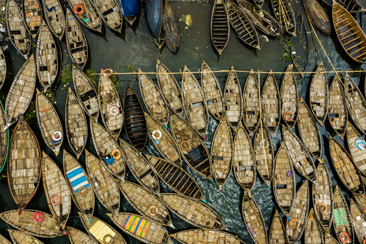 Aerial view of numerous wooden boats moored closely together in the river featuring textured wooden decks and lifebuoys in Dhaka Dhaka Division Bangladesh.