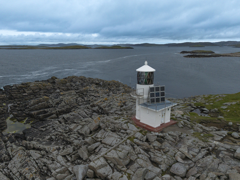 Aerial view of Fugla Ness Lighthouse on a rugged rocky coastline with solar panels overlooking the sea Hamnavoe Scotland United Kingdom.