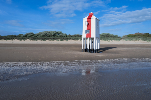Aerial view of the iconic Burnham on Sea Low Lighthouse standing on its wooden stilts on the sandy beach under a clear blue sky in Burnham on Sea England United Kingdom.
