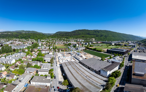 Aerial view of the construction site at Biel Bienne Bozingenfeld Champ with industrial warehouses residential houses and green hills under a clear blue sky Biel Bienne Canton of Bern Switzerland.
