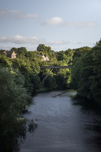 View of the modern footbridge spanning the River Wear surrounded by lush green trees and historic buildings in Durham England United Kingdom. View of the modern footbridge spanning the River Wear surrounded by lush green trees and historic buildings in Durham England United Kingdom.