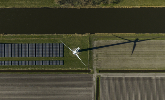 Aerial view of a wind turbine casting a long shadow over solar panels and agricultural fields next to a canal Netherlands. Aerial view of a wind turbine casting a long shadow over solar panels and agricultural fields next to a canal Netherlands.