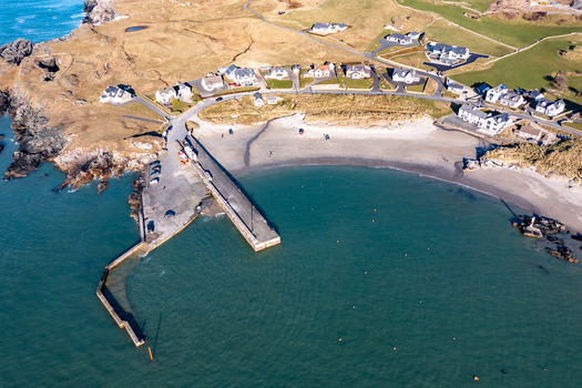 Aerial view of Portnablagh harbour and sandy beach with surrounding coastal houses green fields and rocky shoreline in Portnablagh County Donegal Ireland. Aerial view of Portnablagh harbour and sandy beach with surrounding coastal houses green fields and rocky shoreline in Portnablagh County Donegal Ireland.