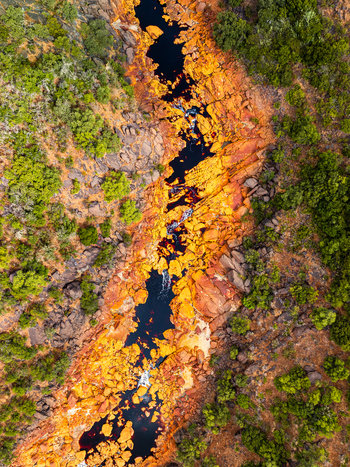 Aerial view of the winding Rio Tinto river flowing through vibrant orange and red mineral rich rocky terrain surrounded by lush green vegetation in Andalusia Spain. Aerial view of the winding Rio Tinto river flowing through vibrant orange and red mineral rich rocky terrain surrounded by lush green vegetation in Andalusia Spain.
