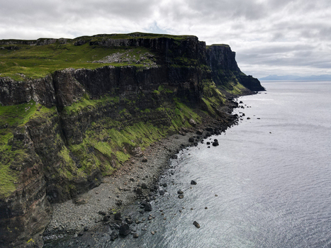 Aerial view of the dramatic dark cliffs and rocky shoreline of Talisker Bay Beach under a cloudy sky in Isle of Skye United Kingdom.