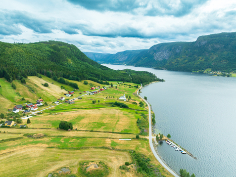 Aerial view of the village of Araksbo with traditional houses green fields and a small harbor along the lake Araksbo Agder Norway.