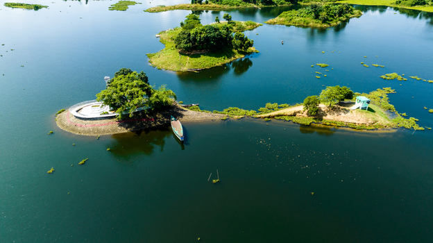 Aerial view of small islands with lush green trees and a wooden boat moored in the calm blue waters of Kaptai Lake in Rangamati Chittagong Division Bangladesh.