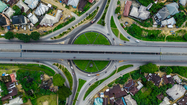 Aerial view of a large roundabout with a central green space and an elevated highway bridge crossing over it surrounded by residential buildings and vegetation in Uyo Akwa Ibom Nigeria. Aerial view of a large roundabout with a central green space and an elevated highway bridge crossing over it surrounded by residential buildings and vegetation in Uyo Akwa Ibom Nigeria.