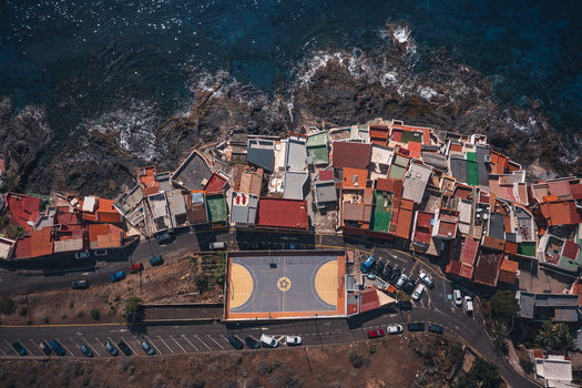 Aerial view of the colorful houses and rocky coastline of the village with a basketball court and the blue sea Bocacangrejo Canarias Spain. Aerial view of the colorful houses and rocky coastline of the village with a basketball court and the blue sea Bocacangrejo Canarias Spain.