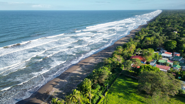 Aerial view of the meeting of deep blue ocean waves with a dark sandy beach and the vibrant green forest stretching along the coastline Tortuguero Limón Province Costa Rica. Aerial view of the meeting of deep blue ocean waves with a dark sandy beach and the vibrant green forest stretching along the coastline Tortuguero Limón Province Costa Rica.