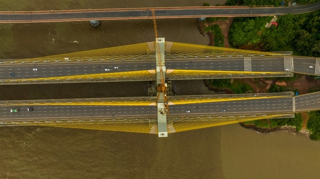 Aerial view of the Zuari Bridge with its yellow cable stayed structure spanning the river featuring multi lane traffic and construction cranes in Cortalim Goa India.