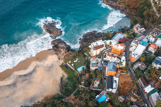 Aerial view of the Vizhinjam coastline featuring sandy beaches rocky outcrops turquoise sea waves and coastal buildings nestled among palm trees in Kovalam Keralam India. Aerial view of the Vizhinjam coastline featuring sandy beaches rocky outcrops turquoise sea waves and coastal buildings nestled among palm trees in Kovalam Keralam India.