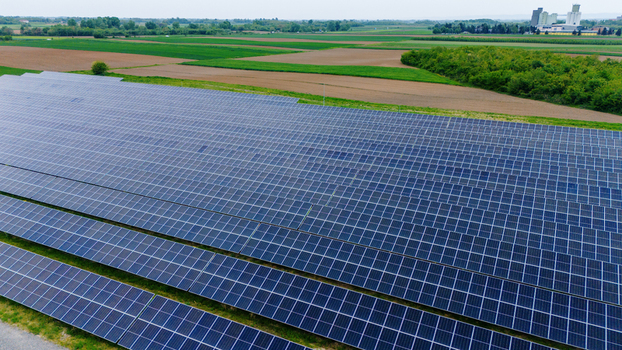 Aerial view of a large solar panel farm surrounded by agricultural fields and green trees under a bright sky in Sabac Vojvodina Serbia.