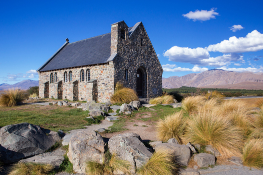 View of The Church of the Good Shepherd surrounded by tussock grass and rocky terrain with mountains in the background in Lake Tekapo Canterbury Region New Zealand.