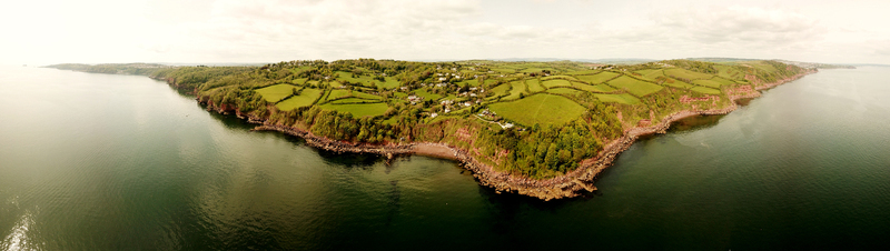 Aerial view of the rugged coastline featuring lush green fields divided by hedgerows and steep cliffs overlooking the calm sea in Devon England United Kingdom.