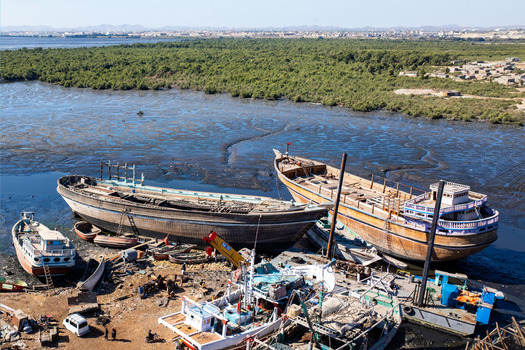 View of traditional wooden fishing boats under construction and repair at Karachi Fish Harbour with lush mangrove forests and coastal landscape in Karachi Sindh Pakistan.
