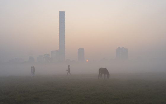 View of a foggy morning unveils silhouettes of a person horse and distant skyscrapers where the sun barely peaks Kolkata West Bengal India. View of a foggy morning unveils silhouettes of a person horse and distant skyscrapers where the sun barely peaks Kolkata West Bengal India.