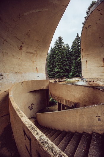 View of the brutalist concrete Korcanica Memorial Zone with its spiral staircase and curved walls surrounded by a pine forest in Sanski Most Federation of Bosnia Bosnia and Herzegovina. View of the brutalist concrete Korcanica Memorial Zone with its spiral staircase and curved walls surrounded by a pine forest in Sanski Most Federation of Bosnia Bosnia and Herzegovina.