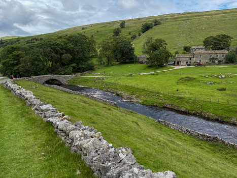 View of a historic stone bridge crossing a river in the Yorkshire Dales surrounded by lush green hills stone walls and traditional farm buildings Hawes England United Kingdom. View of a historic stone bridge crossing a river in the Yorkshire Dales surrounded by lush green hills stone walls and traditional farm buildings Hawes England United Kingdom.