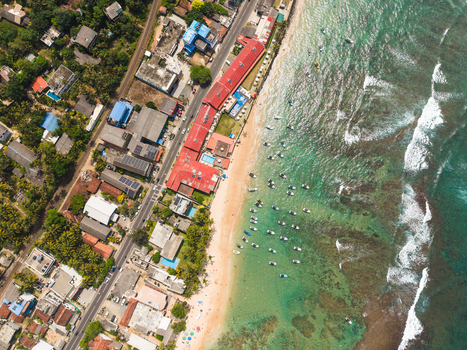 Aerial view of the sandy beach and turquoise ocean with anchored boats and coastal buildings in Hikkaduwa Southern Province Sri Lanka. Aerial view of the sandy beach and turquoise ocean with anchored boats and coastal buildings in Hikkaduwa Southern Province Sri Lanka.