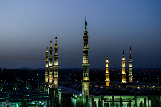 View of the illuminated minarets of Al Masjid e Nabawi at dusk with the mosque complex glowing against the twilight sky in Madinah Al Madinah Province Saudi Arabia.