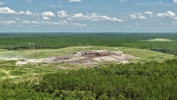Aerial view of Putnam County Central Landfill with heavy machinery operating on the waste mound surrounded by dense pine forests in Palatka Florida United States.