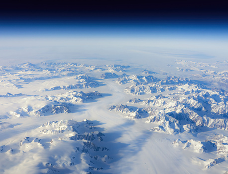 Aerial view of the stark white mountains and glacial valleys meet the hazy horizon under a deep blue sky Narsarsuaq Greenland.