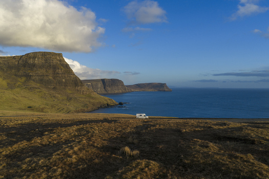 Aerial view of a camper parked on a coastal road overlooking dramatic cliffs and the blue ocean under a bright sky in Isle of Skye. Aerial view of a camper parked on a coastal road overlooking dramatic cliffs and the blue ocean under a bright sky in Isle of Skye.