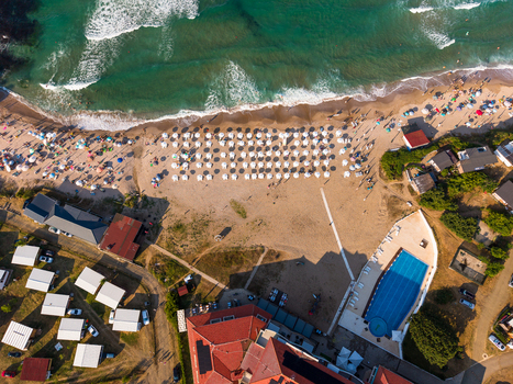 Aerial view of Camping Yug beach with rows of white umbrellas a swimming pool and surrounding buildings along the coastline in Kiten Burgas Bulgaria.