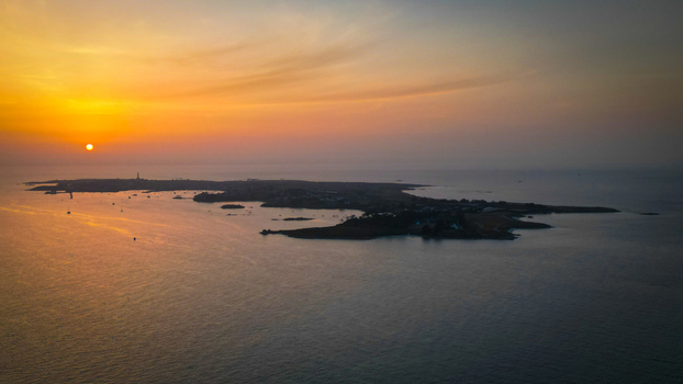 Aerial view of &Icirc;le de Batz basks in the warm glow of the setting sun its silhouette a dark contrast against the fiery sky Roscoff Brittany France.