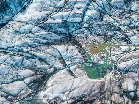 Aerial view of a glacier in Iceland featuring deep crevasses and a vibrant green meltwater pool. Aerial view of a glacier in Iceland featuring deep crevasses and a vibrant green meltwater pool.