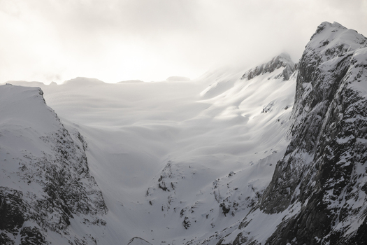 View of snow covered mountain peaks and rugged cliffs under a misty sky with soft sunlight Kvaloya Troms Norway. View of snow covered mountain peaks and rugged cliffs under a misty sky with soft sunlight Kvaloya Troms Norway.