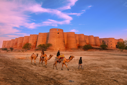 Derawar Punjab Pakistan 31 January 2016 View of Derawar Fort with men riding camels across the desert landscape under a clear sky.