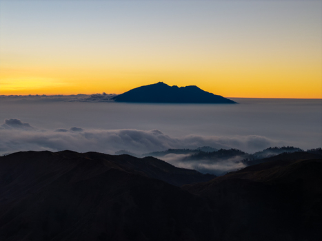 Aerial view of a mountain peak rising above a dense sea of clouds during a golden sunrise in the highlands of East Java Kecamatan Tosari Jawa Timur Indonesia. Aerial view of a mountain peak rising above a dense sea of clouds during a golden sunrise in the highlands of East Java Kecamatan Tosari Jawa Timur Indonesia.