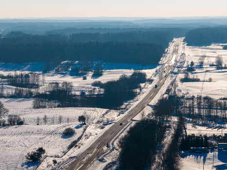 Aerial view of a long highway stretching through a snow covered winter landscape with dense pine forests and open fields Lithuania. Aerial view of a long highway stretching through a snow covered winter landscape with dense pine forests and open fields Lithuania.