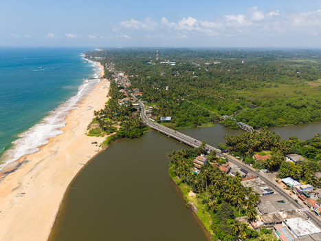 Aerial view of the coastline featuring a bridge over a river sandy beach and lush tropical vegetation in Galle Southern Province Sri Lanka.
