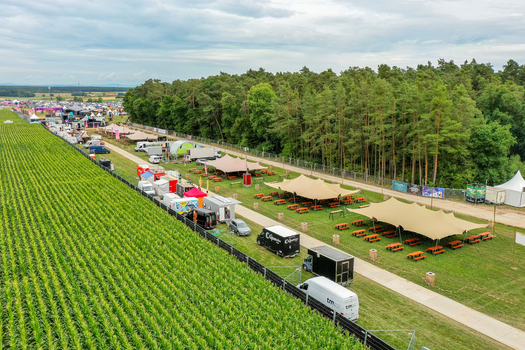 Herzogenaurach Germany 25 July 2025 Aerial view of the Open Beatz Festival grounds featuring event tents food stalls and people near a green forest under a cloudy sky. Herzogenaurach Germany 25 July 2025 Aerial view of the Open Beatz Festival grounds featuring event tents food stalls and people near a green forest under a cloudy sky.