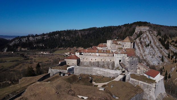 Aerial view of the historic Chateau de Joux fortress perched on a rocky cliff surrounded by rolling hills and forests in La Cluse et Mijoux Bourgogne Franche Comte France. Aerial view of the historic Chateau de Joux fortress perched on a rocky cliff surrounded by rolling hills and forests in La Cluse et Mijoux Bourgogne Franche Comte France.