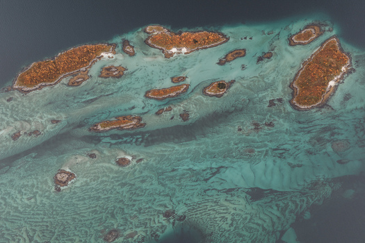 Aerial view of small islands with autumn colored vegetation surrounded by turquoise clear water in Senja Troms Norway.