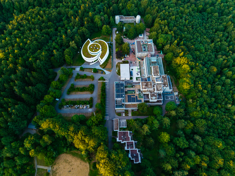 Aerial view of the Max Planck Institute for Astronomy nestled within a dense forest featuring modern research buildings green roofs and parking areas in Heidelberg Baden Wurttemberg Germany.