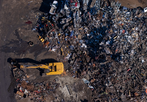 Aerial view of a scrap metal facility with a large yellow excavator working near piles of crushed vehicles and industrial waste in Kalamazoo Michigan United States.