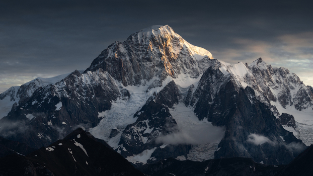 View of the majestic snow covered peaks of the Mont Blanc massif illuminated by golden sunset light under a dramatic sky in Aosta Valley Italy. View of the majestic snow covered peaks of the Mont Blanc massif illuminated by golden sunset light under a dramatic sky in Aosta Valley Italy.