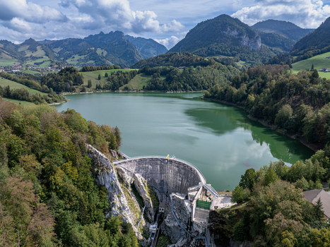 Aerial view of Barrage de Montsalvens a concrete arch dam nestled in lush green hills with the calm reservoir waters reflecting the sky in Chatel sur Montsalvens Fribourg Switzerland. Aerial view of Barrage de Montsalvens a concrete arch dam nestled in lush green hills with the calm reservoir waters reflecting the sky in Chatel sur Montsalvens Fribourg Switzerland.