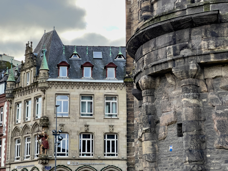 View of the historic Porta Nigra Roman city gate alongside a traditional building with ornate architectural details in Trier Rheinland Pfalz Germany.