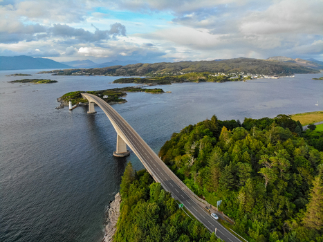 Aerial view of Skye Bridge connecting the mainland to the Isle of Skye featuring lush green trees calm water and a cloudy sky in Isle of Skye Scotland United Kingdom. Aerial view of Skye Bridge connecting the mainland to the Isle of Skye featuring lush green trees calm water and a cloudy sky in Isle of Skye Scotland United Kingdom.